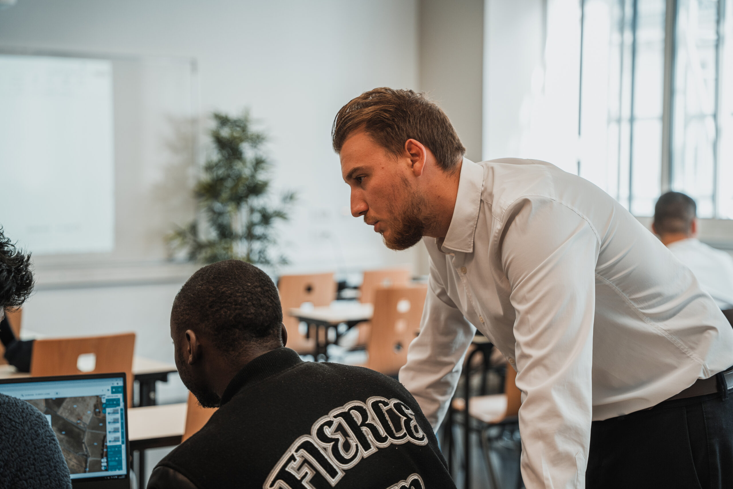 Un homme en chemise se penche sur un étudiant assis pour lui expliquer quelque chose