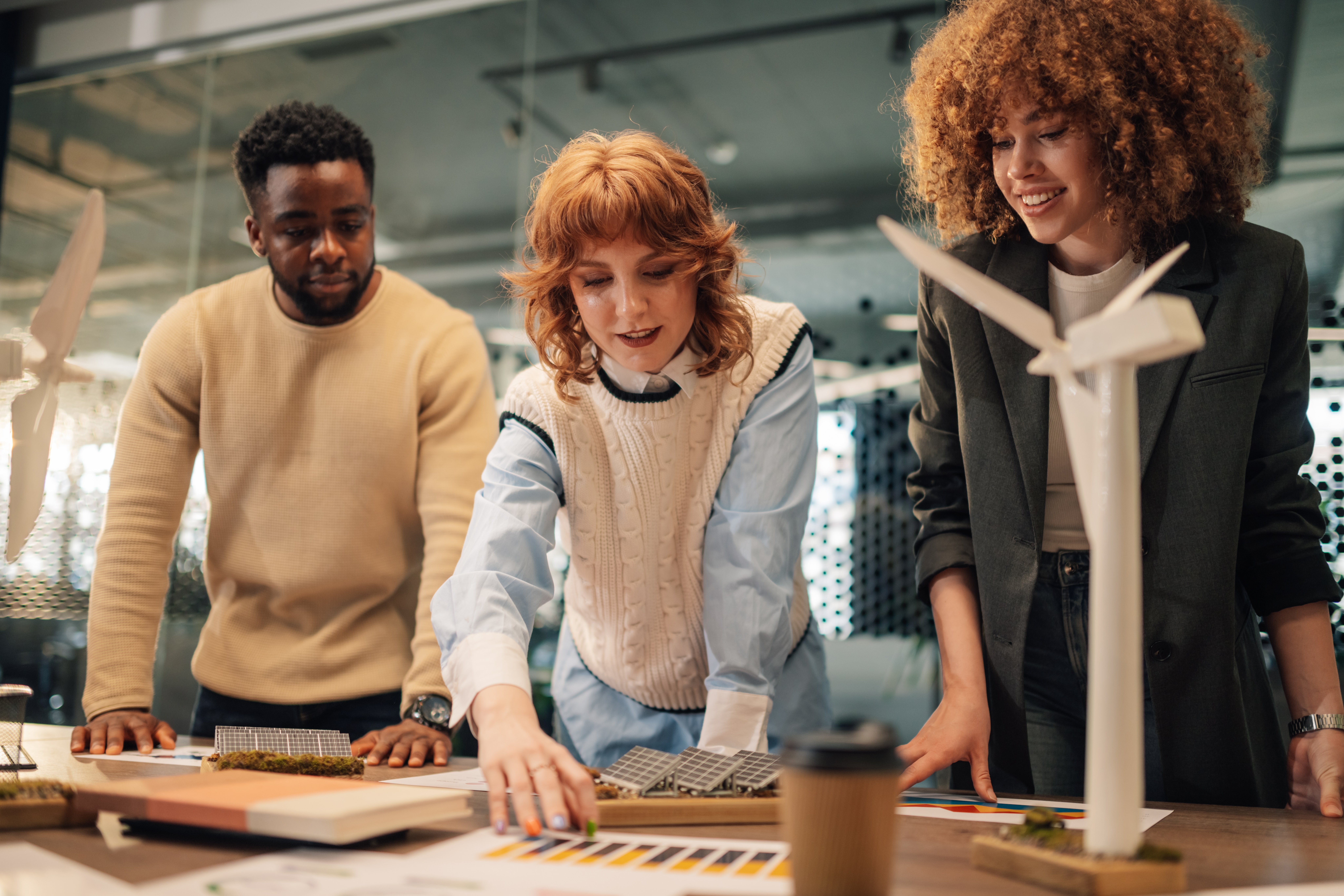 Étudiants ou jeunes professionnels travaillant sur un projet d’énergies renouvelables avec maquettes d’éoliennes et panneaux solaires autour d’une table.